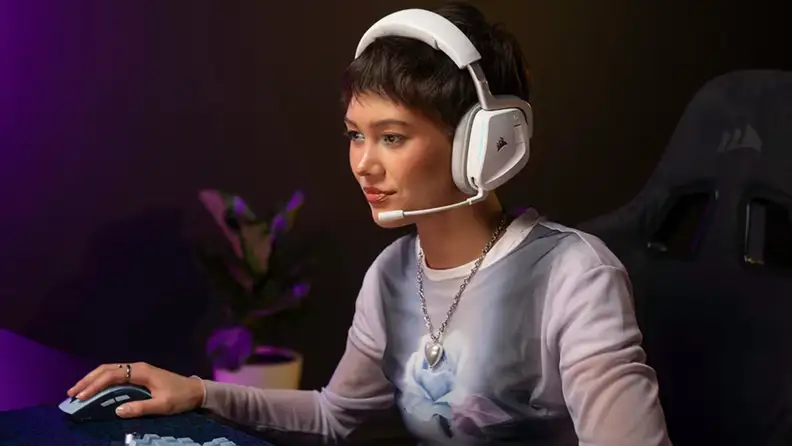 A gamer wears a white Corsair headset while playing at a desktop setup, highlighting the headset’s comfortable design and wireless functionality.