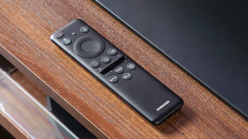 The Samsung remote control sitting on top of a wooden credenza.