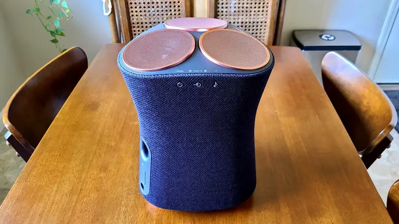 Sony SRS-RA5000 sits on a wooden kitchen table, its hour-glass shape lit with sunlight and revealing its controls