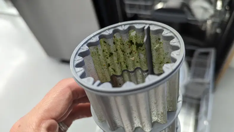 A close-up of the Bosch dishwasher's filter, which is filled with tiny green particles.