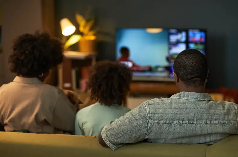 Back view of one mother, father, and child sitting on a couch watching TV.
