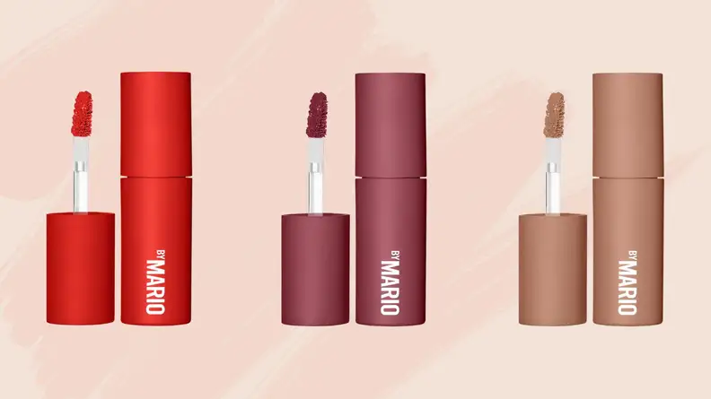 Red-, plum-, and beige-colored lipstick tubes with doe-foot applicators stand against a pink background.