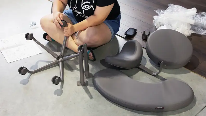 Person assembling the Pipersong Meditation Chair on ground.