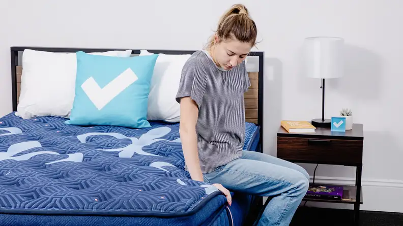 A person sitting on the edge of a mattress.