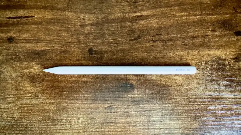 A photo of the Apple Pencil Pro sitting ona wooden desktop.