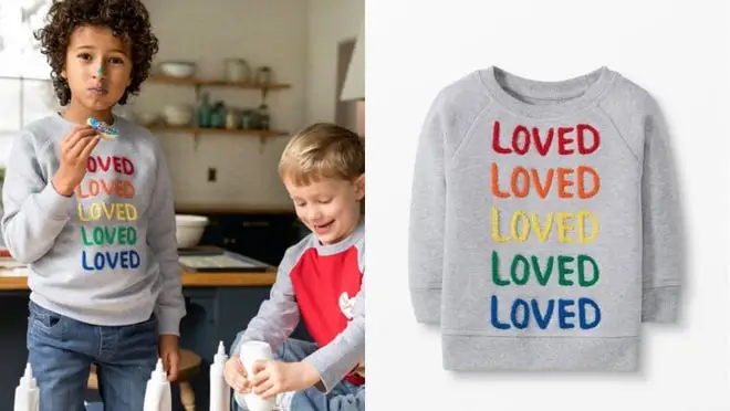 Child wearing gray crew neck with rainbow writing that reads "LOVED."