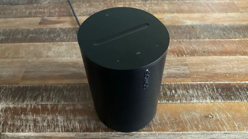 The Sonos Era 100 speaker on a wooden surface shot from above to show the controls on top.