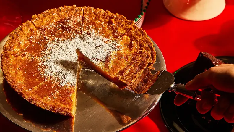 A hand removing a slice of pie from the full pie