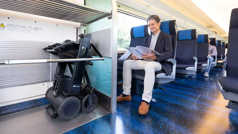 A person rides a train with their wheelchair folded on the side.