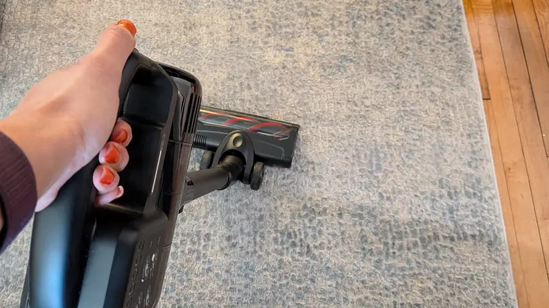 A hand holding a stick vacuum on a carpet