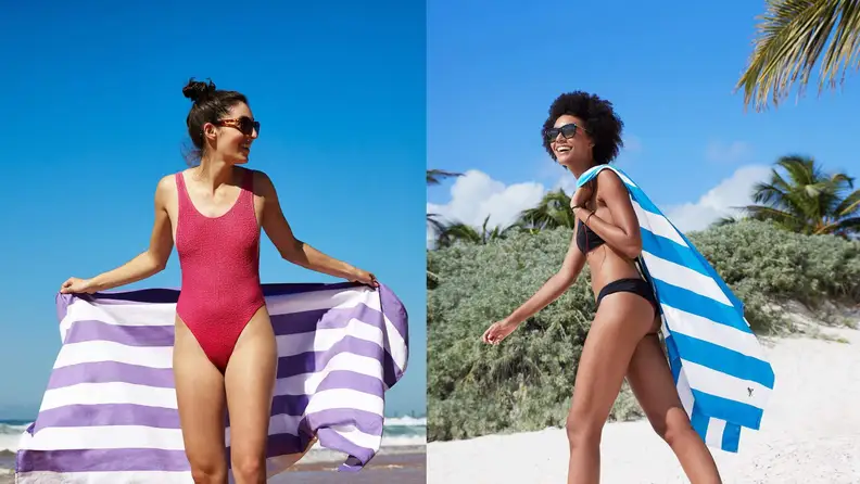 Woman standing on the beach with striped towel draped behind them.