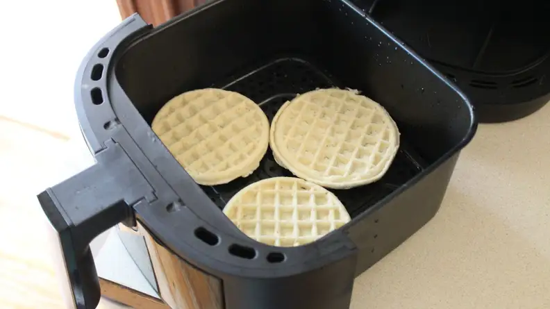 Three frozen waffles placed inside of basket of the Kalorik 5-Quart Digital Air Fryer on top of kitchen counter.