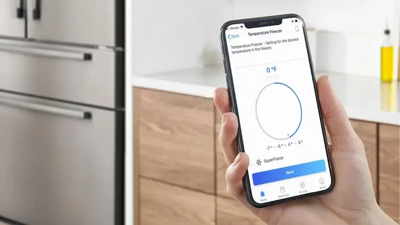 Person holding up smart phone with freezer temperature settings on screen through the Bosch Home Connect app in front of kitchen cabinets.