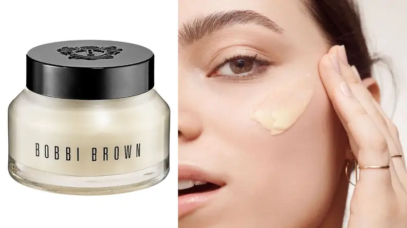 On the left: The tub of Bobbi Brown Vitamin Enriched Face Base Priming Moisturizer sits on a white background. On the right: A person applies the cream-colored Bobbi Brown Vitamin Enriched Face Base Priming Moisturizer to their cheekbone.