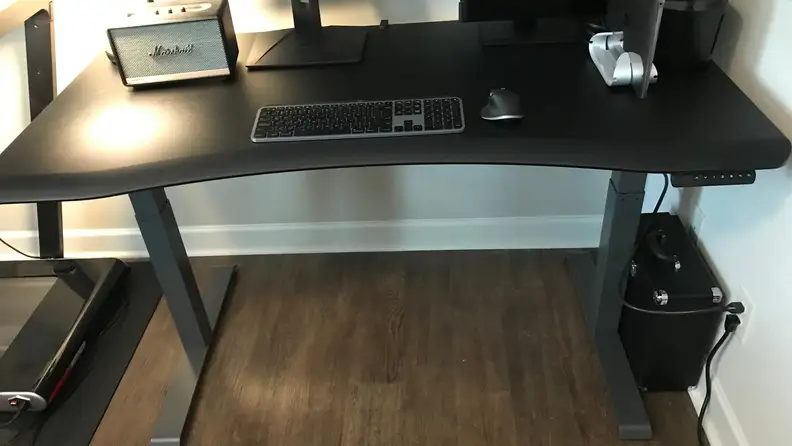 A computer desk with two monitors, a speaker, and keyboard in a living room.