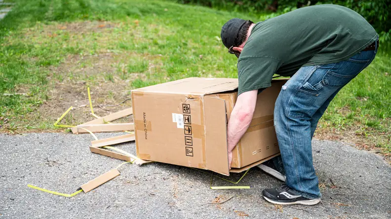 A person lifts a generator out of a cardboard box outside.