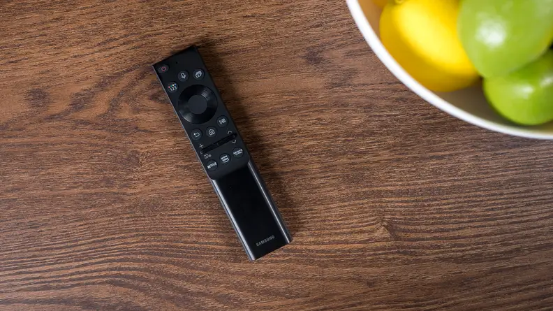 The TV's remote sits on a table near a bowl of fruit