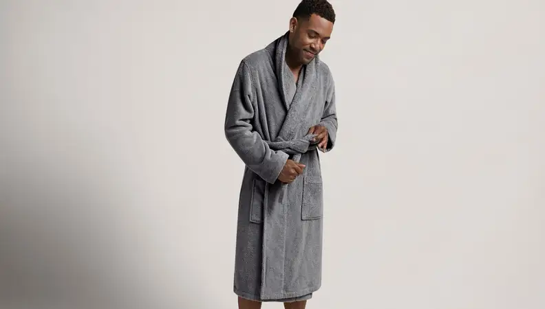 Man in knee length gray robe on a gray background.