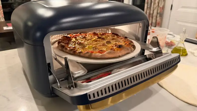 Countertop electric pizza oven baking a freshly cooked pizza on a stone inside the oven chamber.
