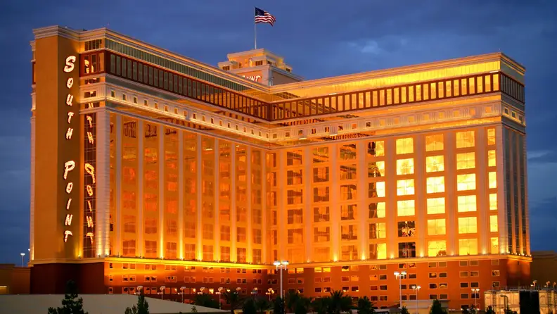 South Point Hotel, Casino & Spa exterior illuminated in warm golden lighting at dusk, with the resort’s name displayed vertically along the building.