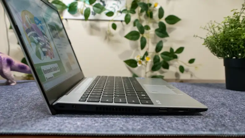 A shot of the laptop from the side, with the dinosaur peeking over the lid.