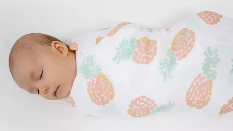 Sleeping baby wrapped in an Aden + Anais swaddle blanket with a pineapple pattern.