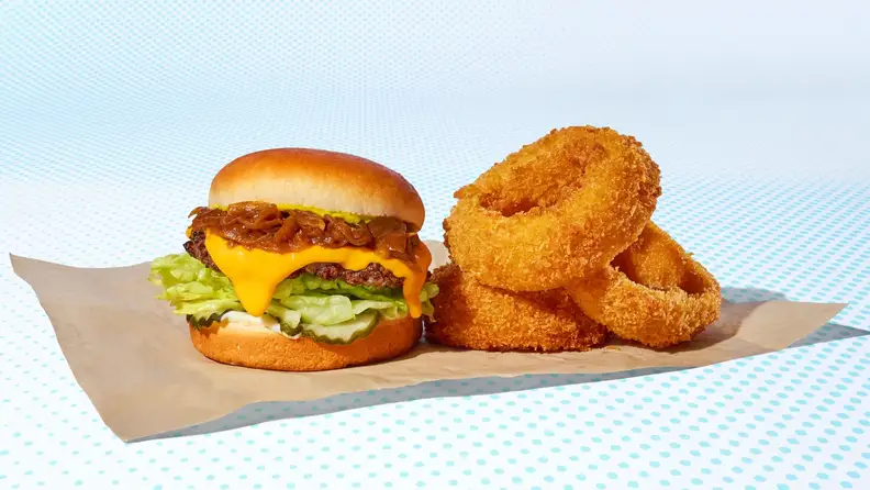 A burger topped with caramelized onions and cheese, next to onion rings