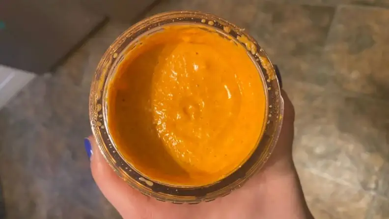 Hand holds cup with orange blended smoothie inside.