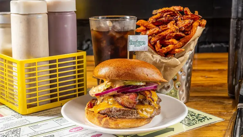 A loaded bacon cheeseburger with sweet potato fries and a soda