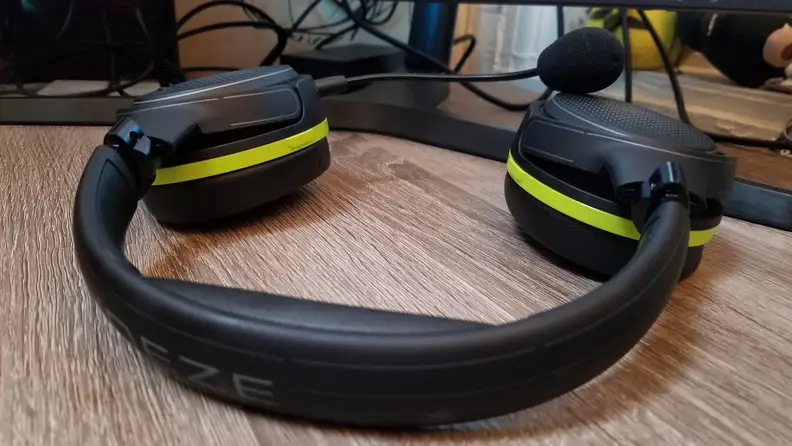 A gaming headset rests on a desktop with the earphones facing down.