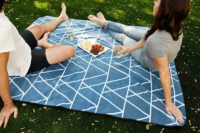 Two people sitting on a blue outdoor blanket on grass.