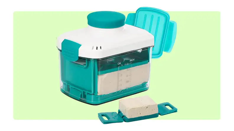 Product shot of the Noya tofu press with a small block of tofu next to it.