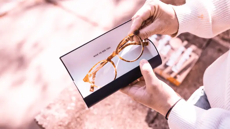 A person pulls out a pair of eyeglasses from inside its case.