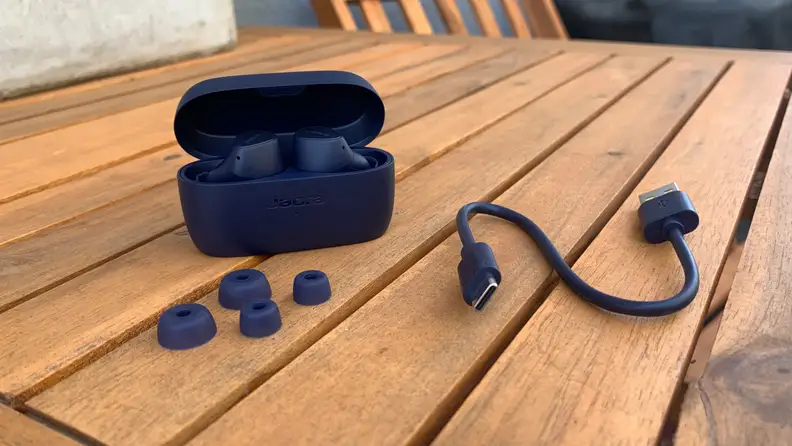 The Jabra Elite 4 earbuds outside a black and next to a black USB cord on a table.