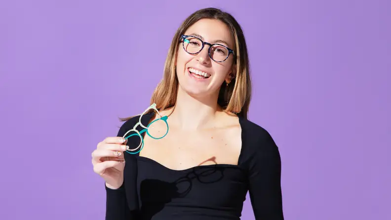 Woman wearing black shirt and smiling in pair of eyeglasses in front of purple background