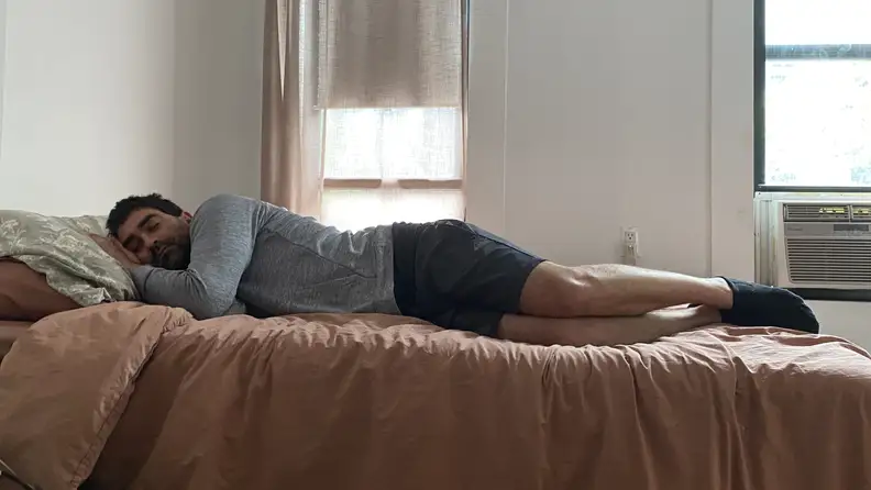 Man laying on his side on top of Ziwi bed with peach mattress.
