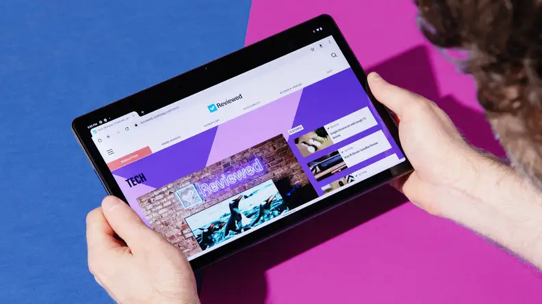 A man holds the Lenovo Tab P10 Plus Gen 3 with both hands, blocking two of the speakers in  the tablet's quad-speaker array.