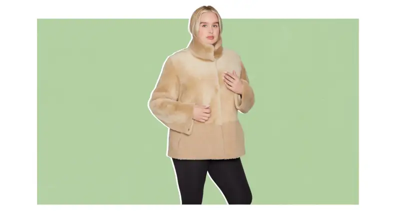 A model wearing a khaki-colored shearling jacket that has two textures on the top and bottom halves.