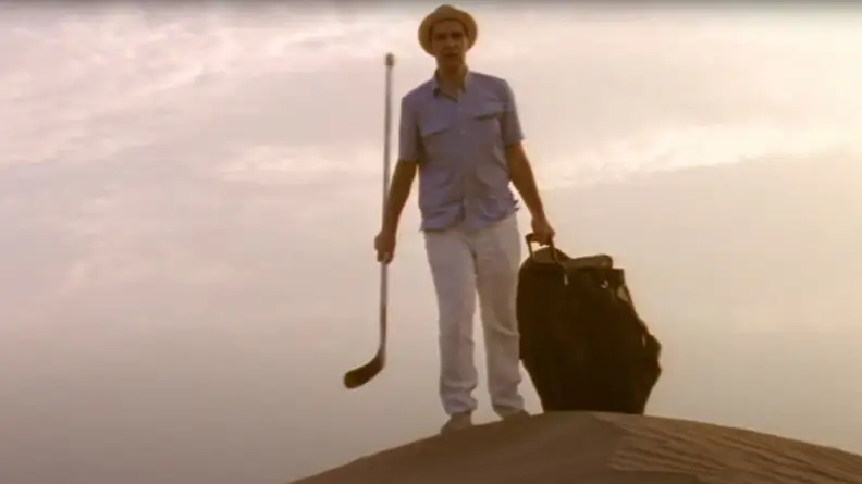 A man walking in the desert with a bag and a hockey stick