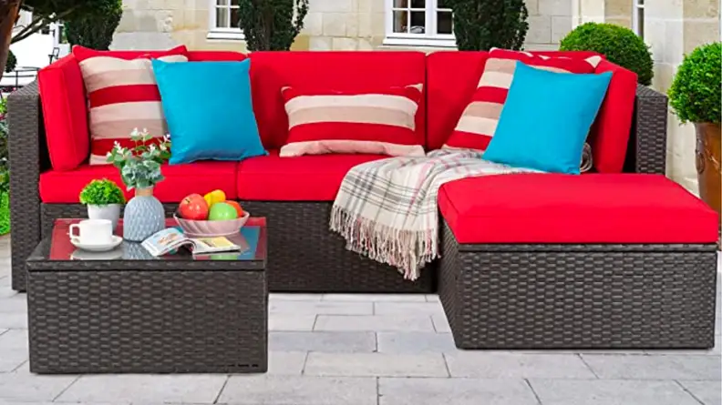 An image of a red-cushioned sectional three-seater sofa with an extended ottoman, next to a brown wicker coffee table.