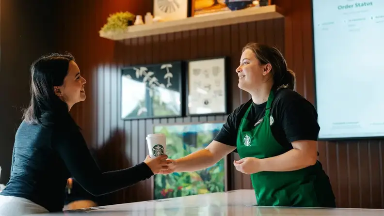 Barista handing a coffee cup to a customer at counter