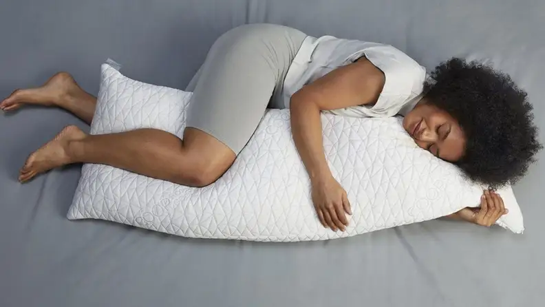 a woman curls up on her side with a body pillow