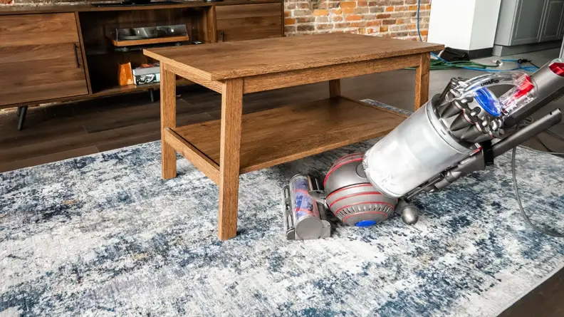 The Dyson Animal 3 on blue carpet attempting to vacuum under a coffee table.