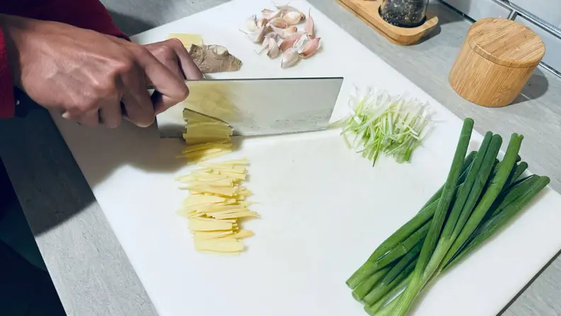 A person's hands cutting vegetables using a cutting board and a cleaver knife.
