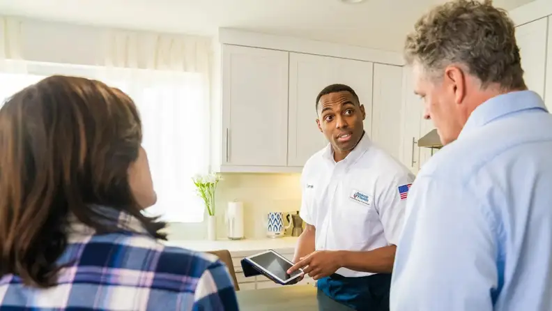Technician using a tablet while speaking with homeowners in kitchen
