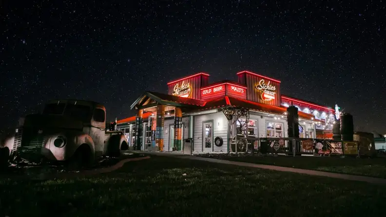 Exterior of Sickies Garage lit up with neon signs at night