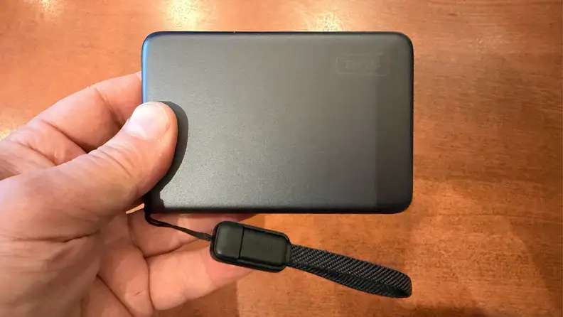 INIU SnapGo Air Power Bank held in a left hand with loop attached, held over a wooden surface.