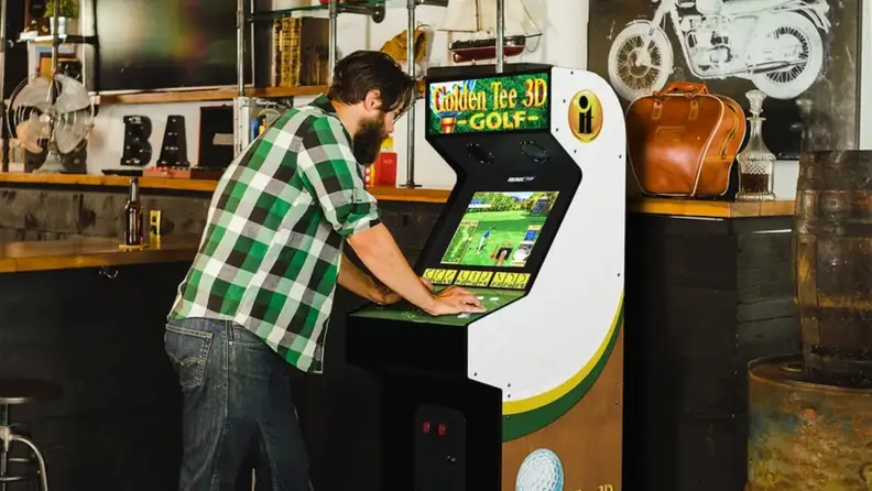 A person playing the Golden Tee 3D Golf arcade cabinet at a bar.