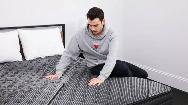 The mattress's tester sitting on the edge of the mattress and pressing down on the center.