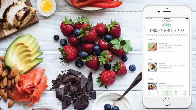 Nibs of chocolate, berries, and sliced avocado on table next to phone with PlateJoy app on it.